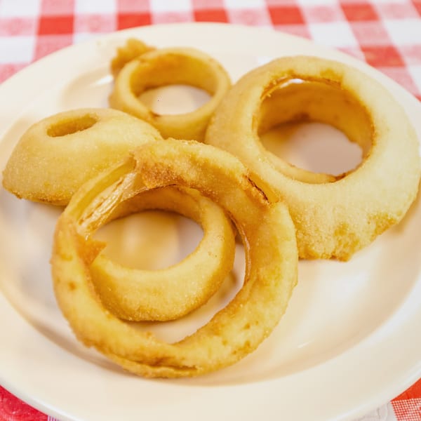 Golden-brown onion rings on a white plate, set against a red and white checkered tablecloth.