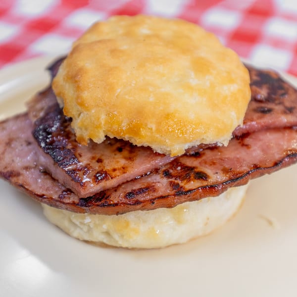 Close-up of a golden-brown biscuit sandwich with grilled meat on a white plate and red checkered background.
