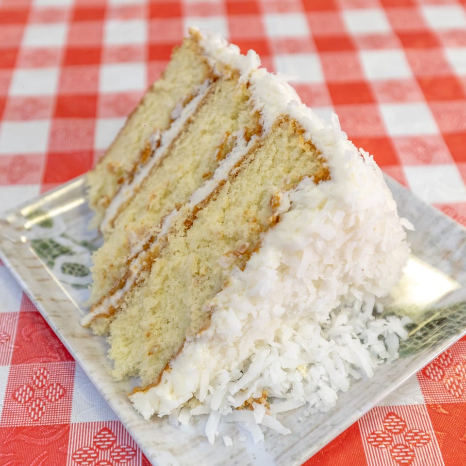 A slice of coconut cake with white frosting and shredded coconut on a plate.