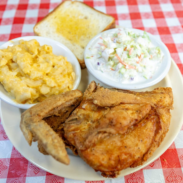 Fried chicken, macaroni and cheese, coleslaw, and toast on a plate with a red and white checkered tablecloth.