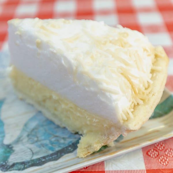 A slice of coconut cream pie with shredded coconut on top, on a patterned plate.