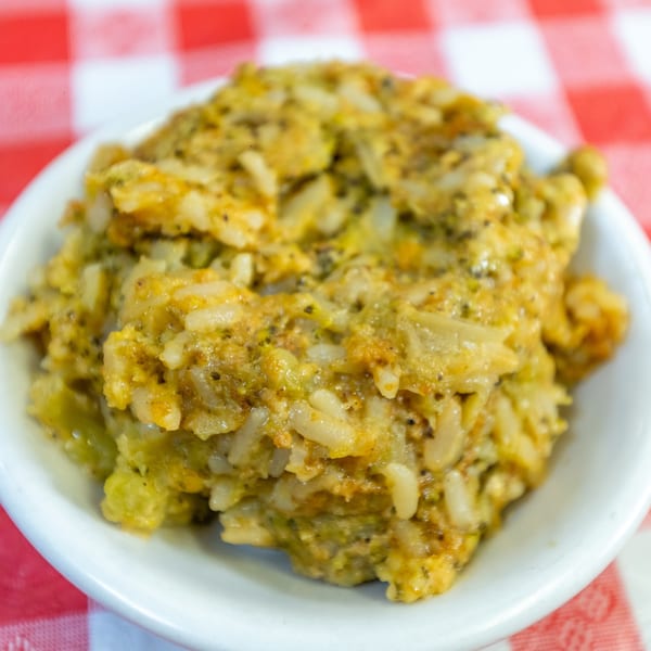 A close-up of a white bowl filled with creamy, green and yellow rice, on a red and white checkered tablecloth.